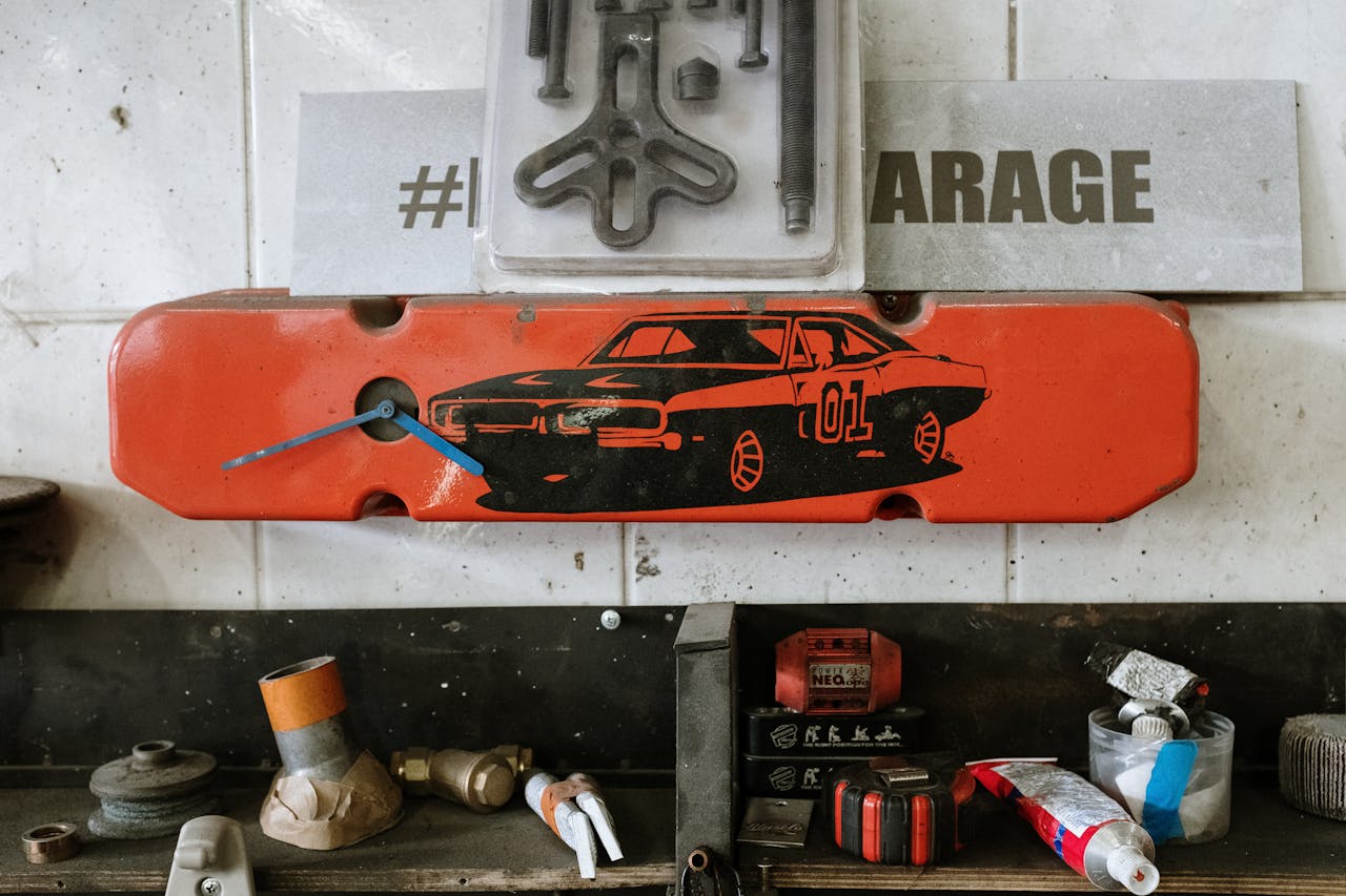 Red car part with a clock on a garage wall, surrounded by tools and auto parts.